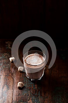 Glass of chocolate milkshake on dark wooden background.