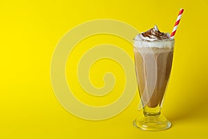 Glass of chocolate milkshake with straw on yellow background