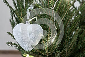 Glass Christmas toy in the shape of a heart hangs on a Christmas tree. A symbol of fragility of love.