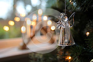 Glass Christmas tree decoration hanging near a window with a traditional candle arch or bridge in blurred background