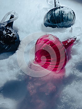 Glass, Christmas tree toys lying on the snow are covered with snowflakes, illuminated by the evening light.