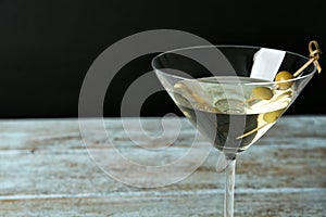 Glass of Classic Dry Martini with olives on wooden table against black background, closeup