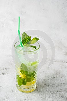 Glass with classic mojito cocktail with lemon and mint, cold refreshing drink or beverage with ice on bright marble background.