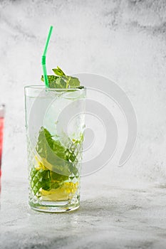 Glass with classic mojito cocktail with lemon and mint, cold refreshing drink or beverage with ice on bright marble background.