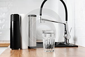 A glass of clean fresh water and set of filter cartridges on wooden table in a kitchen interior. Installation of reverse