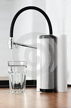 A glass of clean fresh water and set of filter cartridges on wooden table in a kitchen interior. Installation of reverse