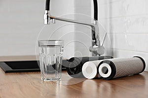 A glass of clean fresh water and set of filter cartridges on wooden table in a kitchen interior. Installation of reverse
