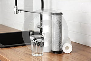 A glass of clean fresh water and set of filter cartridges on wooden table in a kitchen interior. Installation of reverse photo