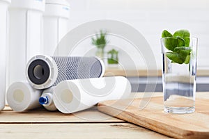 A glass of clean water with osmosis filter and cartridges in a kitchen interior. Concept Household filtration system