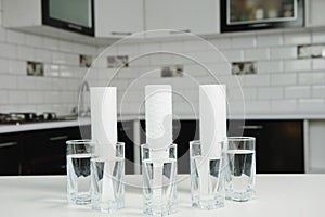 A glass of clean water with osmosis filter and cartridges on white table in a kitchen interior. Concept Household filtration