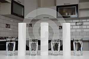 A glass of clean water with osmosis filter and cartridges on white table in a kitchen interior. Concept Household filtration