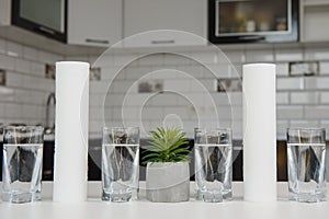 A glass of clean water with osmosis filter and cartridges on white table in a kitchen interior. Concept Household filtration