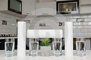 A glass of clean water with osmosis filter and cartridges on white table in a kitchen interior. Concept Household filtration