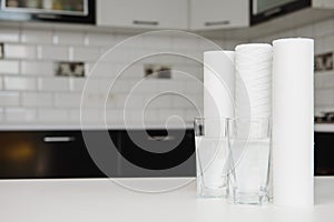 A glass of clean water with osmosis filter and cartridges on white table in a kitchen interior. Concept Household filtration