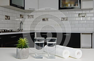 A glass of clean water with osmosis filter, green leaves and cartridges on wooden table in a kitchen interior. Concept Household