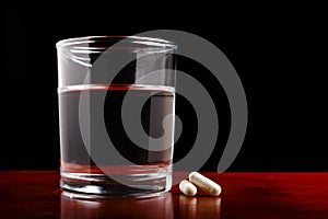 Glass of clear water and pills on dark