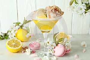 Glass of cocktail, ingredients and flowers against wooden background