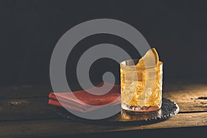 Glass of the cocktail negroni with red napkin and black stone tray on a old wooden board. Decorated orange slice. Nice romantic