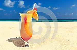 Glass of cocktail is on sandy coral beach