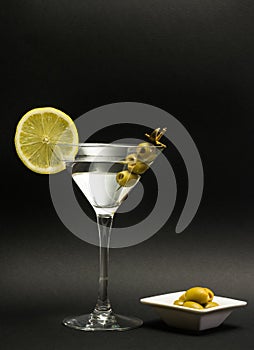 Glass of vodka martini white transparent alcoholic cocktail drink with olives and lemon on the black background.