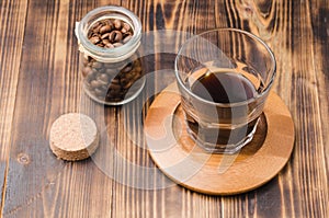 Glass of cofee with cofee beans. Top view. Cup of black coffee in a glass and grains in a glass jar on a wooden table