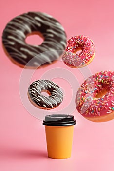 A glass of coffee and levitating donuts on a pink background