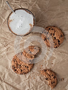 Glass of coffee with milk or latte on a paper background, next to oatmeal cookies. Top view, vertical orientation. Shallow depth