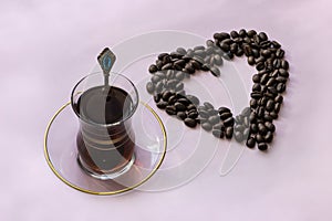 Glass coffee mug and roasted coffee beans on pink background. Coffee mania, love of coffee, concept