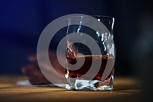 A glass of cognac and a bar of chocolate on a wooden table on a dark background