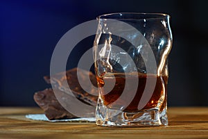 A glass of cognac and a bar of chocolate on a wooden table on a dark background