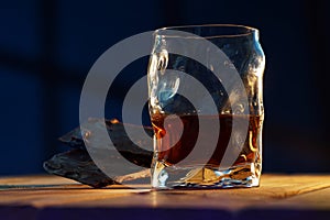 A glass of cognac and a bar of chocolate on a wooden table on a dark background