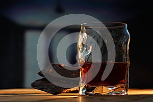 A glass of cognac and a bar of chocolate on a wooden table on a dark background