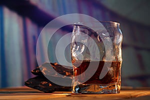 A glass of cognac and a bar of chocolate on a wooden table on a dark background