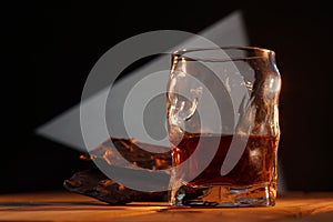 A glass of cognac and a bar of chocolate on a wooden table on a dark background