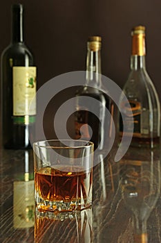 Glass of cognac, brandy or whiscy on mirror table. bottles in a bar on the background