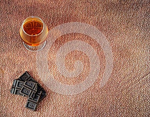 A glass of cognac and a few pieces of chocolate on a brown abstract background