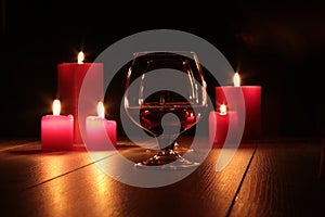 Glass of cognac and red candle on a wooden background