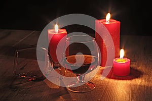 Glass of cognac and red candle on a wooden background