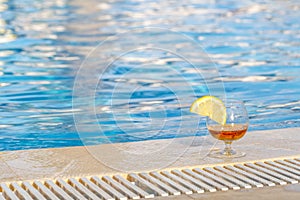 Glass of cognac, a slice of lemon, blue pool water as an attribute of a luxurious holiday