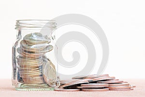 Glass of coin and spread coin on floor on vintage blurred background - Saving money concept.