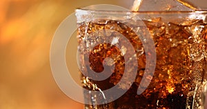 Glass of Cola with ice cubes close-up. Cola drink with Ice and bubbles in glass closeup. Rotating glass of Cola drink over blurred