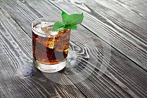 Glass of cola with ice and fresh mint on wooden table.