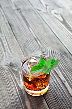 Glass of cola with ice and fresh mint on wooden table.