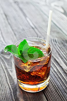 Glass of cola with ice and fresh mint on wooden table.