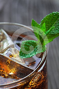 Glass of cola with ice and fresh mint on wooden table.