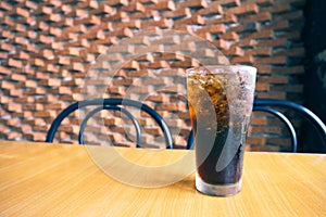 A glass of cola with ice on the table with background brick wall