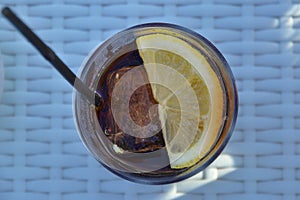 Glass of cola with a slice of lemon, a straw an ice cubes, view from top