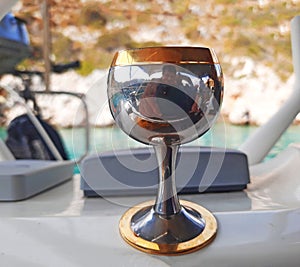 A glass with a cold alcoholic drink on the deck of a yacht during a summer sea vacation on a sunny day against a blurred