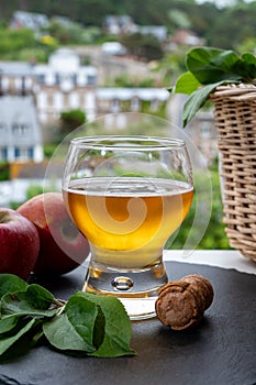 Glass of cold apple cider drink and houses of Etretat village on background, Normandy, France