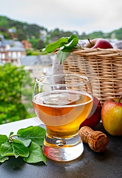 Glass of cold apple cider drink and houses of Etretat village on background, Normandy, France